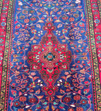 A vibrant, hand-knotted Persian rug with a central medallion floral design, featuring a variety of colors including indigo blue, red, mustard, pink, green, and brown.
