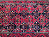 A close-up of a tribal Persian Quchan rug 3.1x2.1m rug with a vibrant red field, dark navy blue geometric borders, and intricate floral motifs in orange, white, and yellow.