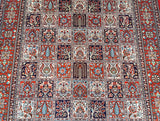 A close-up of a hand-knotted Persian Qum rug featuring a detailed and traditional floral garden design in burnt orange and multiple other colors.