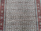 A close-up view of a detailed and ornate Persian Birjand rug featuring geometric patterns with beige, orange, blue, black, brown, pink, and green tones.