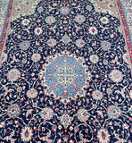 A detailed image of a Persian Sarough rug with a central medallion floral design, featuring a pure lamb's wool pile on a cotton base in various colors including indigo blue, red, beige, and pink.