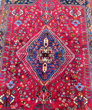 A vibrant Persian Qashqai Shiraz rug with a rich pile of hand-spun wool in a semi-geometric and semi-floral pattern, featuring colors predominantly in red, with accents in blue, brown, green, and black.
