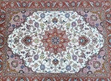 A traditional Persian Tabriz area rug with an intricate floral pattern, featuring a white central field, pink borders, and red corners with blue and green accents.