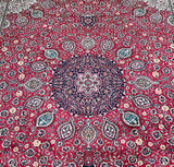 A close-up of a traditional Persian Tabriz area rug with a vibrant red field, featuring a large central navy blue medallion and intricate floral motifs in beige, green, and white.