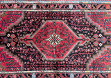 A hand-knotted Persian Tuserkan rug with a geometric medallion design in the center, surrounded by a border with floral patterns. The rug has a variety of colors including black, pinkish red, beige, orange, green, pink, and blue.