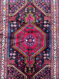 A vibrant, multicolored Persian Tuserkan rug with a geometric medallion design in the center, featuring a variety of colors including black, red, beige, yellow, pink, and blue.