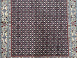 A handcrafted Persian Birjand rug with a Herati design featuring a geometric pattern in beige, black, blue, red, yellow, and pink colors on a white background.