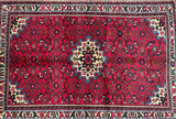 A handcrafted, multicolored Persian rug with a geometric medallion design in the center, featuring a combination of beige, pinkish red, blue, green, and brown tones.