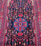 A vibrant, multicolored hand-knotted Persian rug with a geometric tribal design featuring a central medallion floral pattern and vase motifs.
