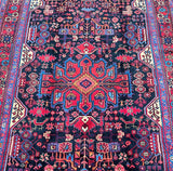 A vibrant, multicolored Persian Nahavand rug with a geometric tribal design, featuring indigo blue, red, beige, and other colors.