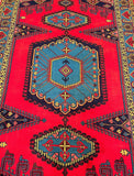 A vintage Persian vis rug featuring a geometric medallion design with animal motifs in burnt orange, red, mustard, and blue tones on a cotton base.
