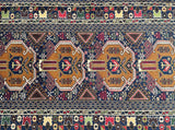 A Afghan Balouchi rug featuring large central medallions in tan and red, surrounded by dark blue, cream, and red geometric borders.