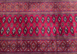 A close-up image of a hand-knotted Persian hall runner featuring a geometric pattern in maroon red, beige, and black tones.