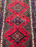 A vibrant, multicolored tribal Persian Hamedan hall runner with an allover geometric diamond medallion design, featuring a red, pink, brown, green, and blue tone dyed pattern.