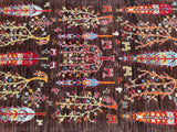 A detailed view of a hand-knotted Afghan Chobi rug featuring a garden design with tree of life motifs in various colors on a brown background.