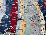 A detailed view of a Gabbeh design hand-knotted super Kazak rug featuring a tribal scenery pattern with various colors like red, blue, yellow, and green.