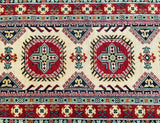 A close-up view of a traditional Kazak-patterned rug featuring geometric designs in beige, blue, yellow, green, and red.