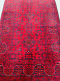 A hand-knotted woolen rug with a geometric and floral pattern in red and burgundy tones.