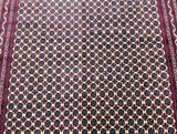 Close-up of a traditional Afghan rug with a geometric tribal pattern in beige, green, orange, black, and burgundy tones.