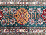 A close-up image of a hand-knotted Afghan Super Kazak hall runner rug with geometric patterns in green, maroon, beige, blue, and mustard tones.