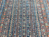 A multicolored geometric patterned woolen rug, featuring a variety of colors including blue, red, and beige, with a traditional shawl design.