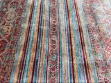 A vibrant, multicolored striped Afghan super kazak rug with a floral pattern, predominantly in shades of blue, red, and beige.