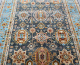 A detailed shot of a traditional Afghan Royal Kazak rug with geometric patterns in shades of blue, gray, green, and terracotta.