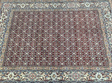 A traditional Persian hand-knotted rug featuring a geometric herati (fishbone) pattern with a border, predominantly in maroon, indigo blue, beige, and other colors.