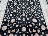 A close-up view of a hand-knotted oriental Jaipur rug featuring a floral design with black, beige, gold, and pink colors on a cotton base.