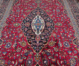 A close-up of an oversize traditional Persian Kashan rug with a central medallion floral design, featuring a mix of red, beige, green, and blue tones.