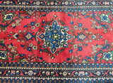 A hand-knotted Persian Afshari rug with a floral design, featuring a red background and bordered with a decorative pattern in blue, green, and beige.