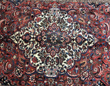 A close-up of a Persian Bakhtiari rug with a bold central medallion floral design, featuring a mix of red, terracotta, beige, blue, brown, and black tones.