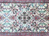 A hand-knotted Persian hall runner rug with a geometric medallion design in beige, pink, light blue, maroon red, green, and black tones, on a cotton base.