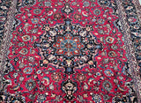 An antique Persian Mashad rug with a deep burgundy and maroon tone, featuring a traditional floral medallion design.