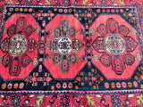 A hand-knotted Persian Zanjan rug with geometric triple medallion tribal design, predominantly in pinkish red and blue tones, on a cotton base.