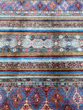 A close-up view of a traditional Kazak rug with a geometric shawl pattern featuring a mix of brown, blue, and red colors.