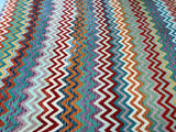A vibrant boho-style kilim rug featuring a geometric pattern in multiple colors, woven from hand-spun wool on a wool base.