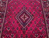 A hand-knotted Persian rug with a deep maroon/burgundy tone, featuring a central medallion semi-geometric semi-floral design.